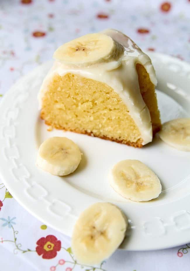 a slice of Banana Pudding Cake glazed with Cream Cheese and topped with sliced bananas in a white plate