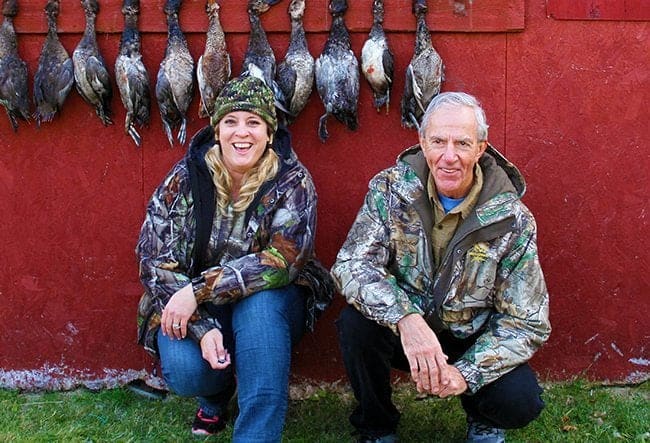daughter and dad in hunting gear with hanging ducks on their background