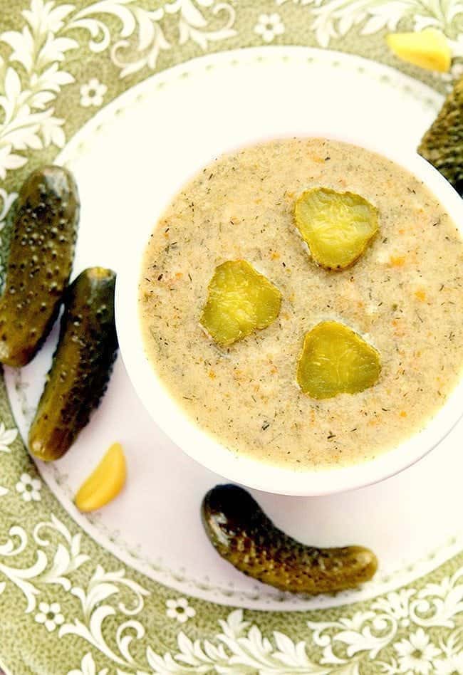 Dill Pickle Soup in a small white round baking dish with some dill pickles around a white plate ready to be enjoy!