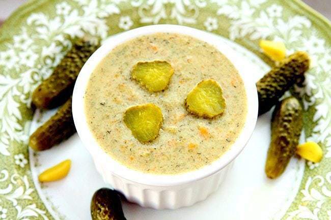 close up shot of Dill Pickle Soup in a small white round baking dish with some dill pickles around a white plate