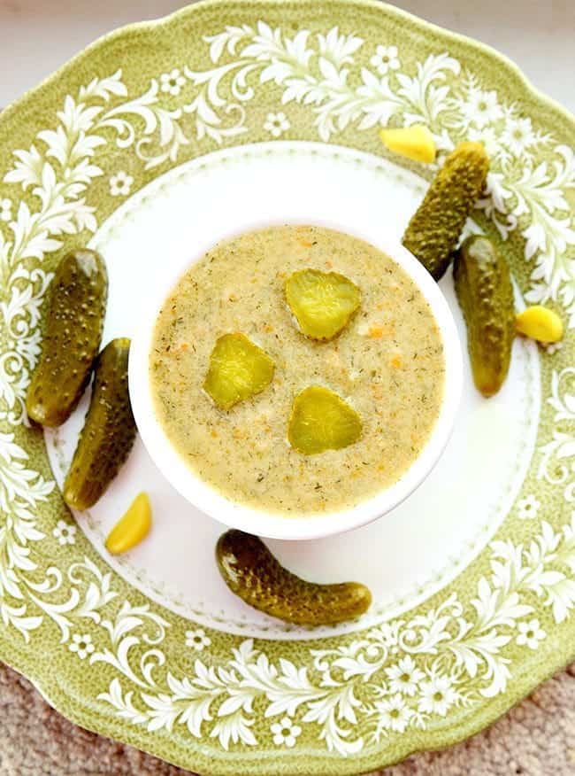 top down shot of Dill Pickle Soup in a small white round baking dish with some dill pickles around a white plate ready to be enjoy!