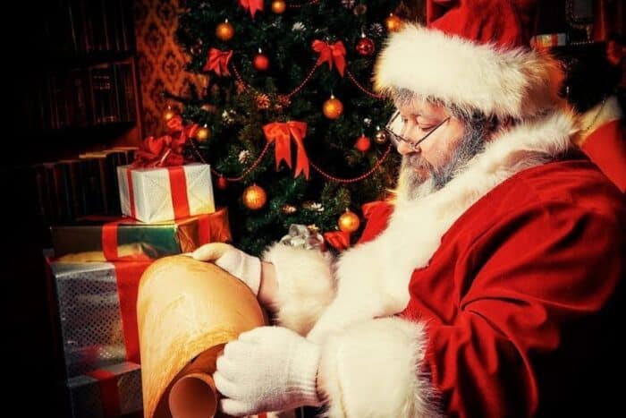 Santa Claus sitting in a room decorated for Christmas, and reading his list