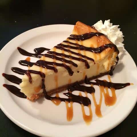 white plate with Diner Cheesecake topped with chocolate and caramel syrup