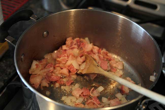  Frying bacon and onions in a large skillet using wooden cooking spoon