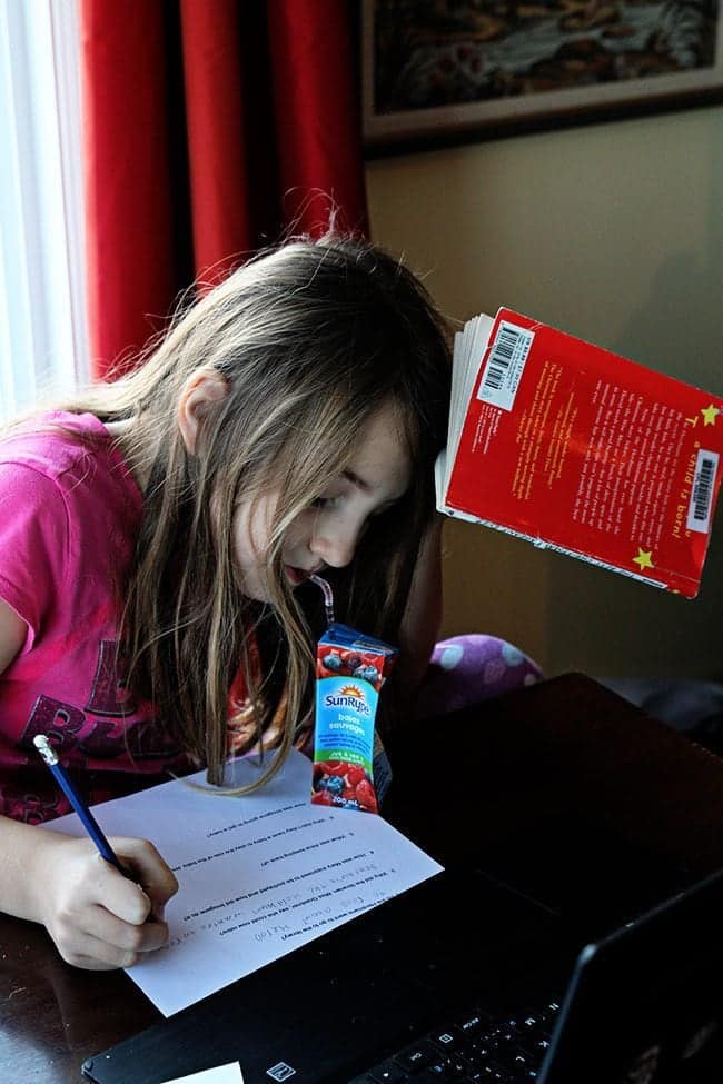 young girl sipping from a box juice while studying and a book was in her head