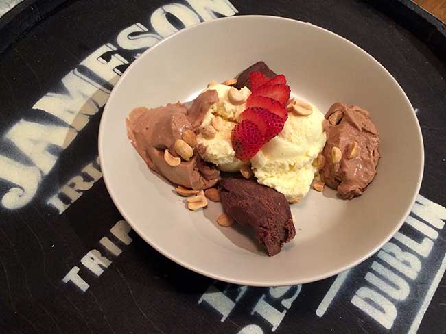 a plate of dessert - chocolate and vanilla ice cream with nuts and slices of strawberries