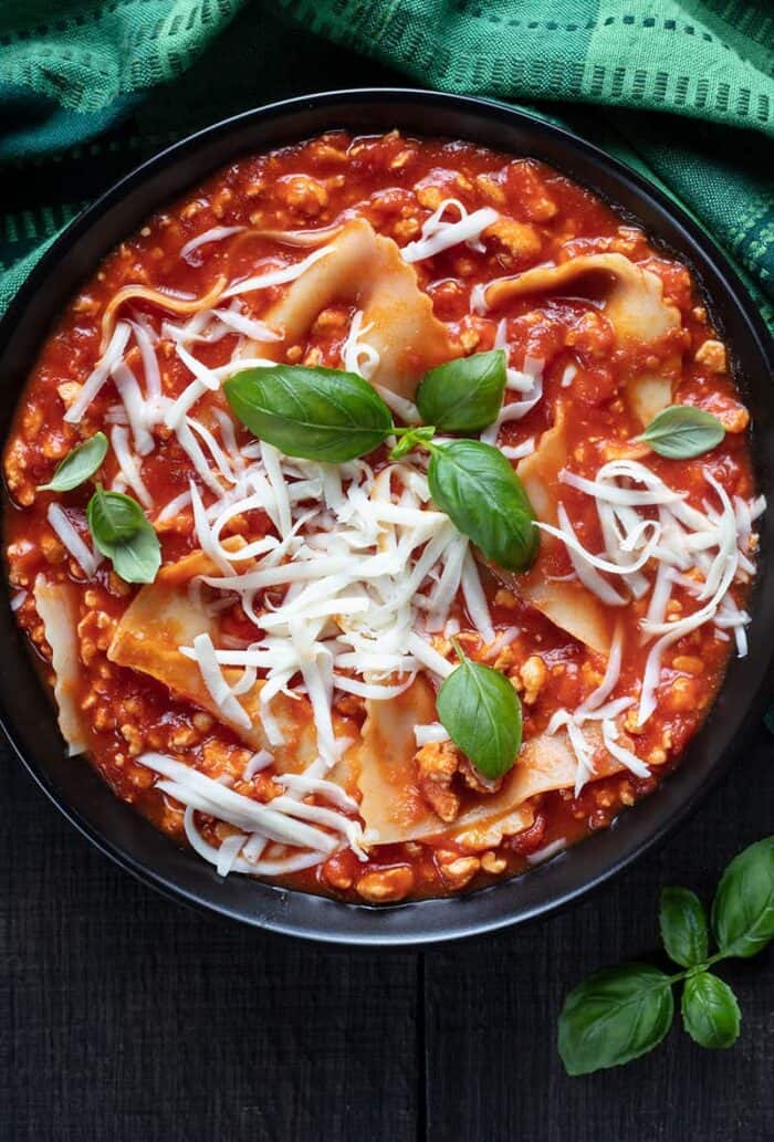 close up large soup bowl with Turkey Lasagna Soup topped with mozzarella cheese, green tablecloth underneath