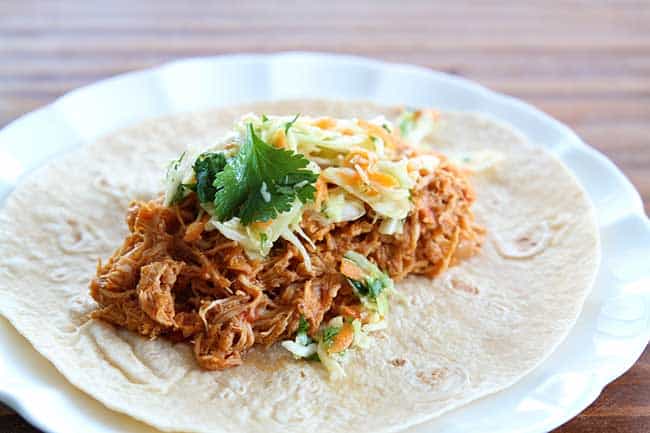 Crock pot Chicken Fajitas served on tortilla topped with Mexican Coleslaw and cilantro in a white plate