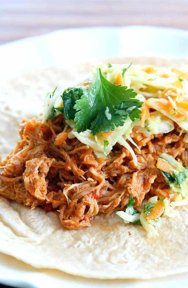 Close up of Crock pot Chicken Fajitas served on tortilla topped with Mexican Coleslaw and cilantro in a white plate