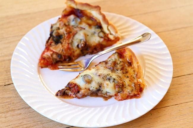 two slices of pizza in a plate with caramelized onions, mushrooms, black olives and pound of cheese on top