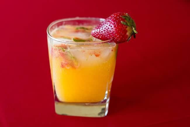Short Glass with Tangerine & Gin garnish with a Piece of Fresh Strawberry on Red Background