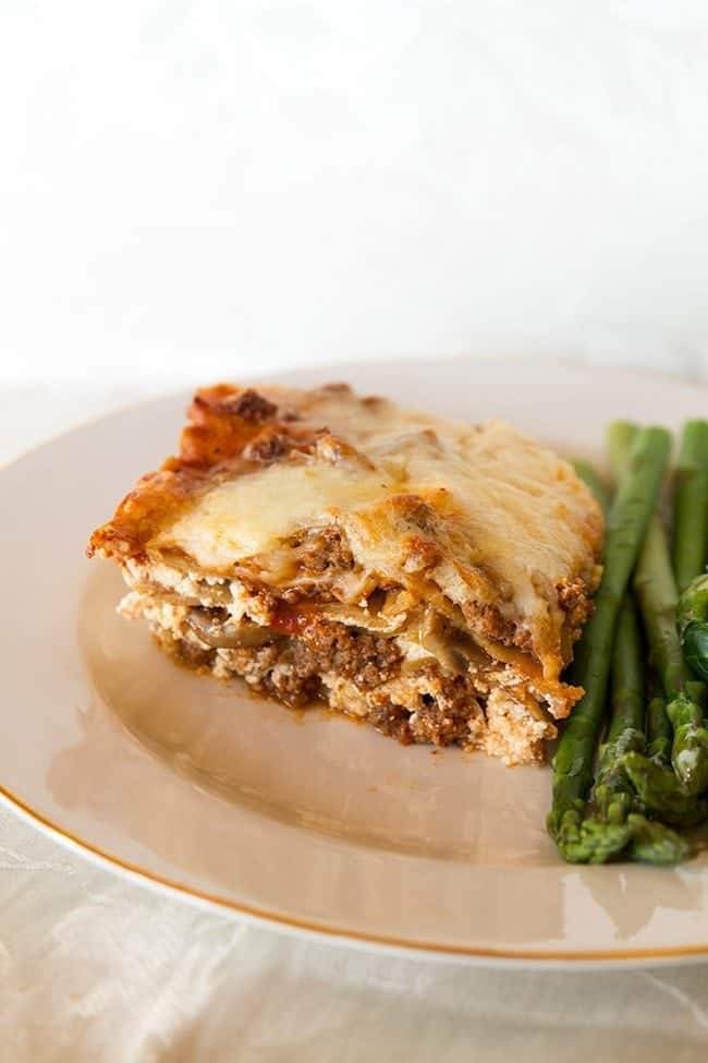 cheesy beef lasagna on a white plate with asparagus