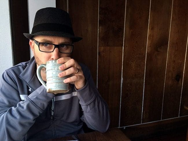 man wearing eyeglasses and jacket, drinking from a mug