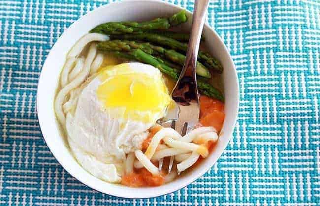 Udon Noodles loaded with poached egg and vegetables on a blue kitchen cloth
