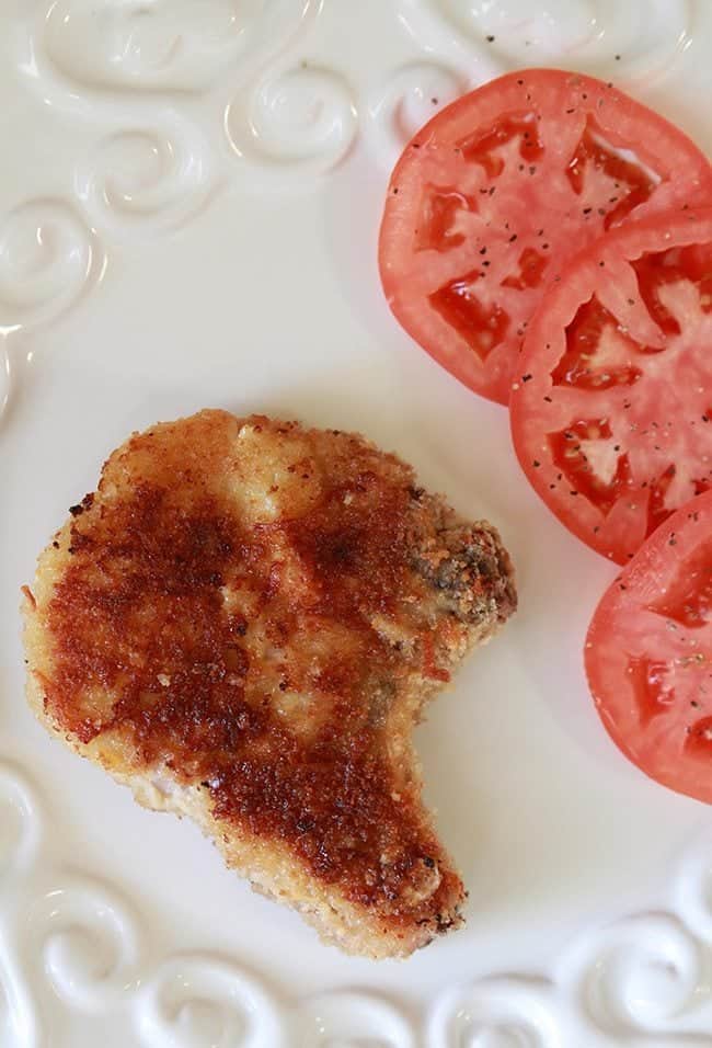 close up of Parmesan Panko Pork Chop garnish with 3 slices of red tomatoes on white background