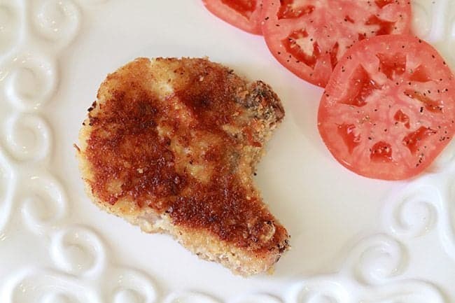 Parmesan Panko Pork Chop garnish with 3 slices of red tomatoes on white background
