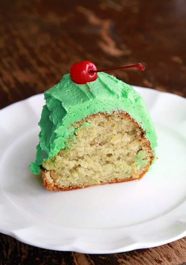 A slice of Watergate Salad Cake with frost and cherry on top in a white plate