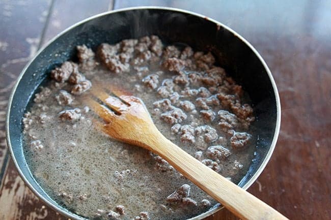 cooking the ground beef in a large skillet using a wooden stir-fry spatula