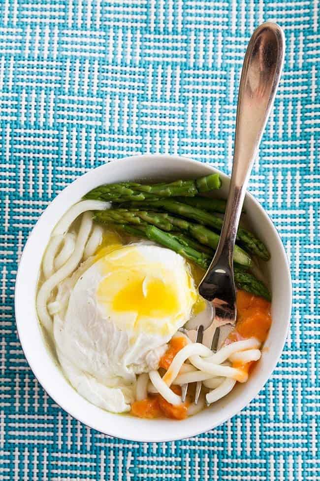 Top down shot of Udon Noodles loaded with poached egg and vegetables with a fork in it