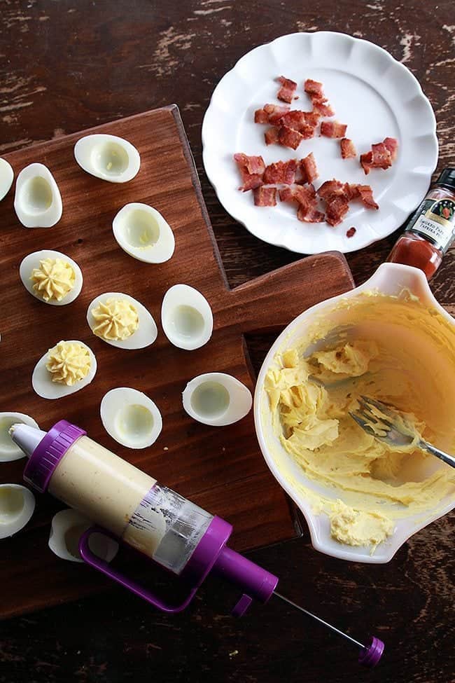 piping the egg yolk filling into the center of each egg, small pieces of bacon on white plate