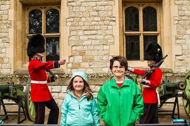 kids standing in the middle of two soldier statues in red uniform