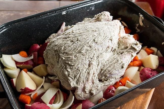 raw chicken covered in herb butter before roasting on top of vegetables in roaster