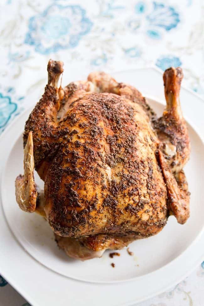 Close up of a whole roast chicken on a white plate