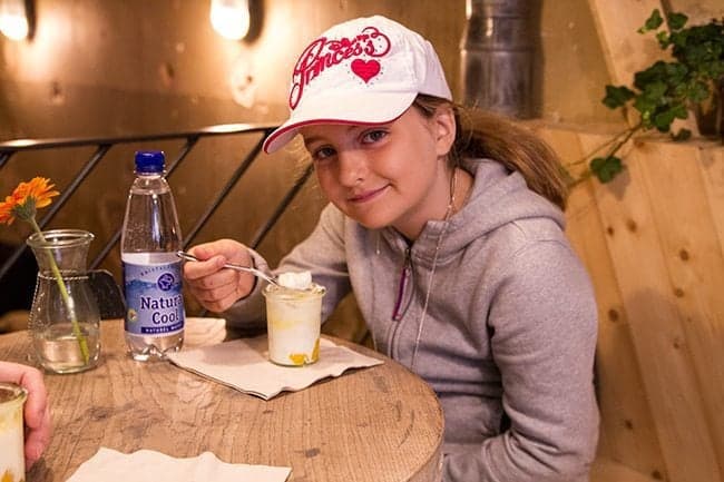 young girl with cap, sitting and enjoying her cup of yogurt beside a bottled water