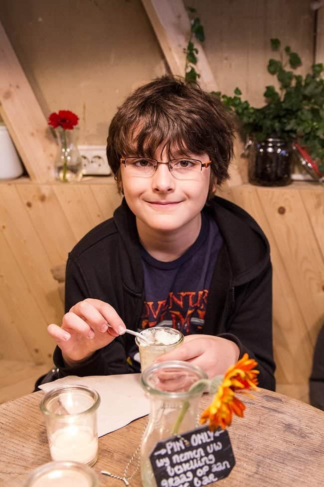 young boy wearing eye glasses, sitting and enjoying his cup of yogurt