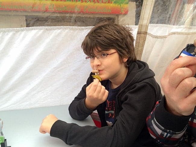 young boy in black jacket trying to eat the herring