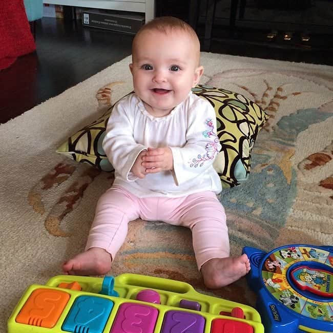 baby girl sitting and smiling with toys and pillow around her