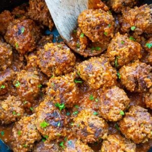 close up porcupine meatballs in a large black skillet with a wooden spoon and some teared parsley leaves