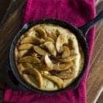 close up of Cinnamon Apple Dutch Baby in a large black skillet over a red kitchen cloth on wood board