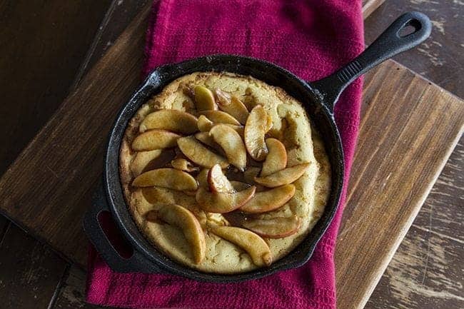 close up of Cinnamon Apple Dutch Baby in a large black skillet over a red kitchen cloth on wood board