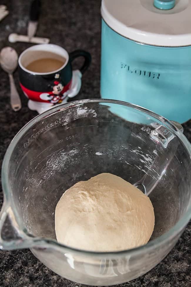 Sweet Dinner Rolls dough rolled into little ball inside Pyrex measuring cup, mickey mug and a large turquoise canister on background