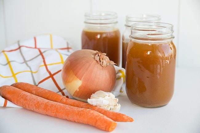 Crock Pot Bone Broth on Jars, Organic Carrots and Onion in kitchen cloth beside it