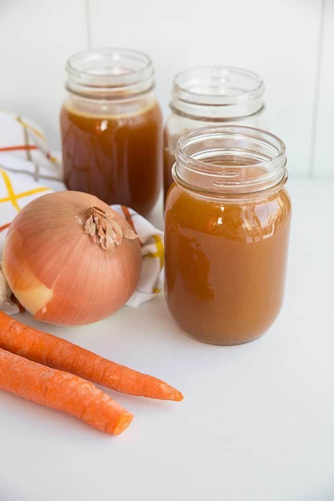 Crock Pot Bone Broth on Jars, Organic Carrots and Onion in kitchen cloth beside it