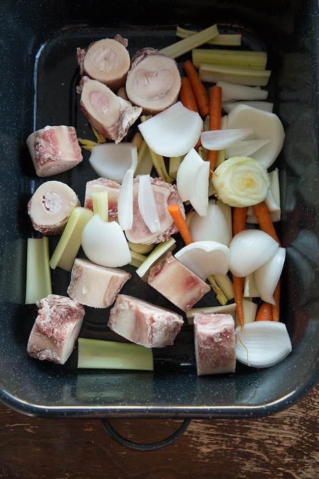 Bones and chopped vegetables in Crockpot ready for roasting