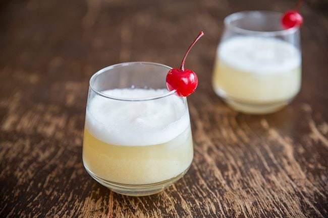 Two glasses of Smoky Whisky Sour Garnish with Cherry on Wood background