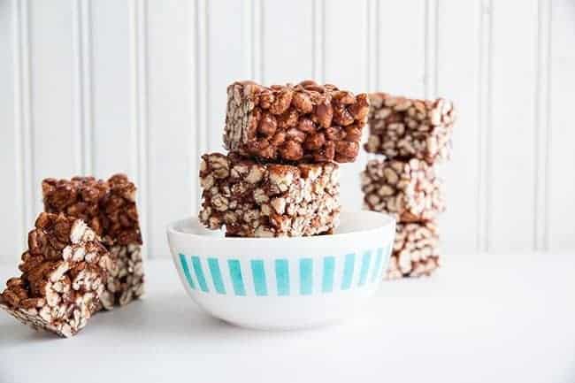 Stacks of Chewy Chocolate Puffed Wheat Squares in White Bowl on White Background