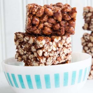 Close up of Stacks of Chewy Chocolate Puffed Wheat Squares in White Bowl on White Background