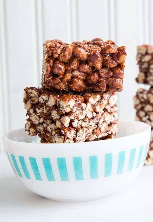Close up of Stacks of Chewy Chocolate Puffed Wheat Squares in White Bowl on White Background