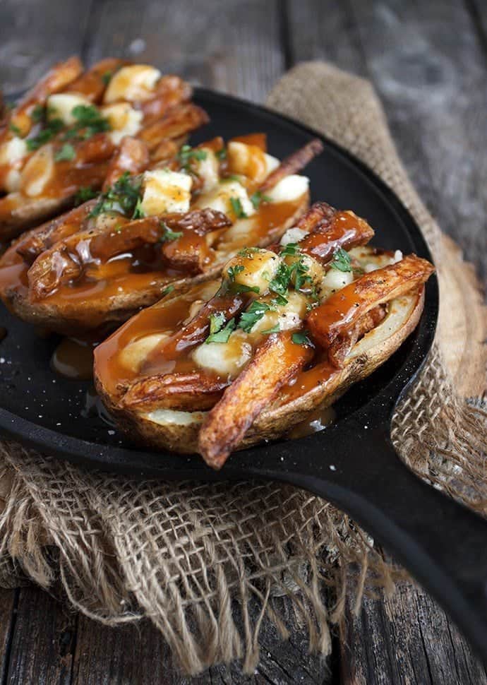 Poutine potato skins in a black skillet topped with Cheese curds and gravy