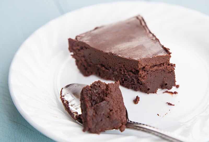 a spoon with Chocolate cake and a slice of Flourless Chocolate Cake in a white plate
