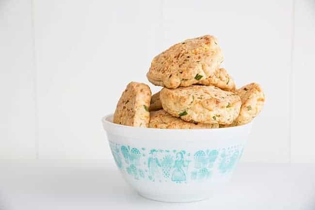 Bumpy shaped Cheddar & Chive Biscuits in white bowl on white background