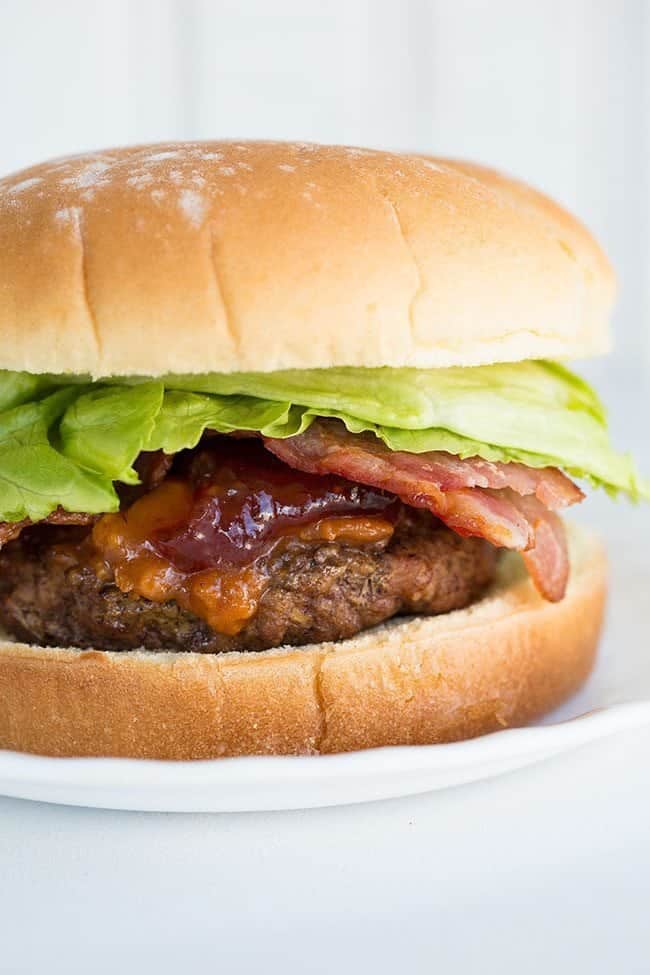 Burger with patty on the bottom of the bun, topped with peanut butter sauce, strawberry jelly and lettuce then the top of the Bun