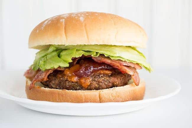 Burger with patty on the bottom of the bun, topped with peanut butter sauce, strawberry jelly and lettuce then the top of the Bun