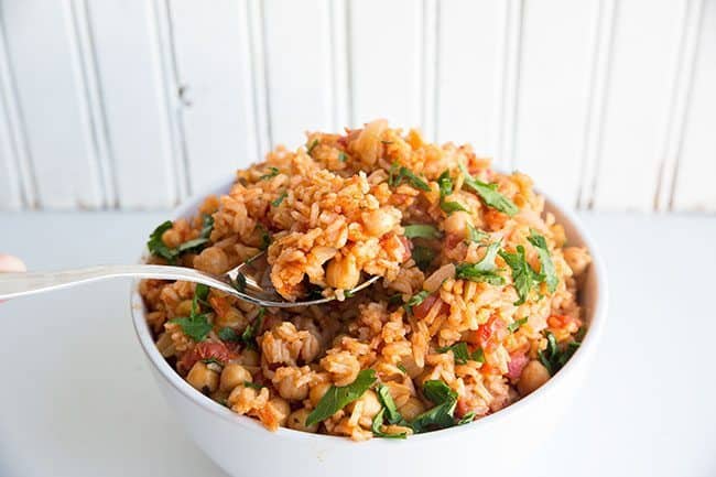  Spooning a Vegan Smoky Spanish Rice & Chickpeas in a white bowl