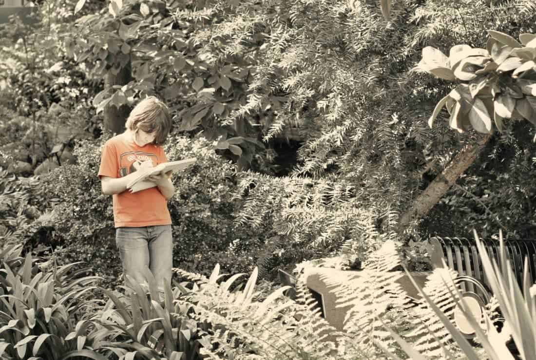 a boy with pen and sketchpad in the middle of garden