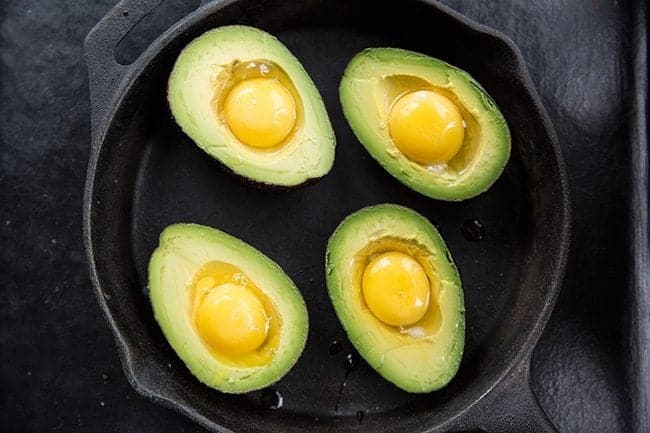 Eggs cracked in each half of avocados